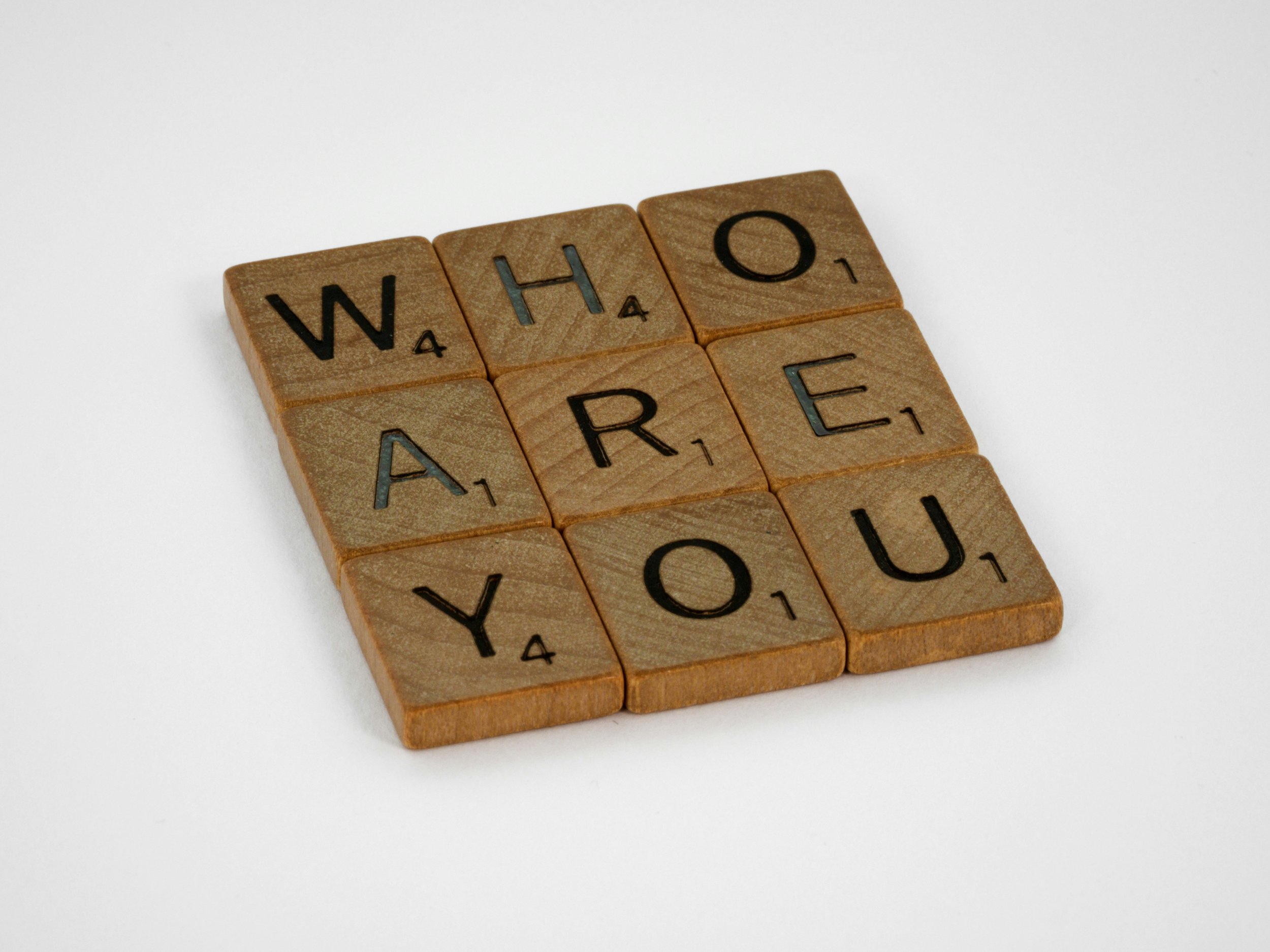 Wooden letter tiles spell out "WHO ARE YOU" on a plain white background.